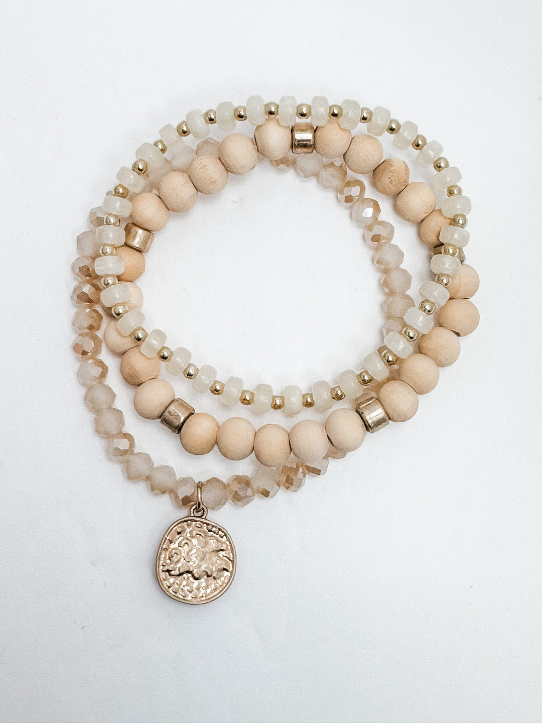 A set of three neutral-colored bracelets with gold coin charm and mixed bead designs.