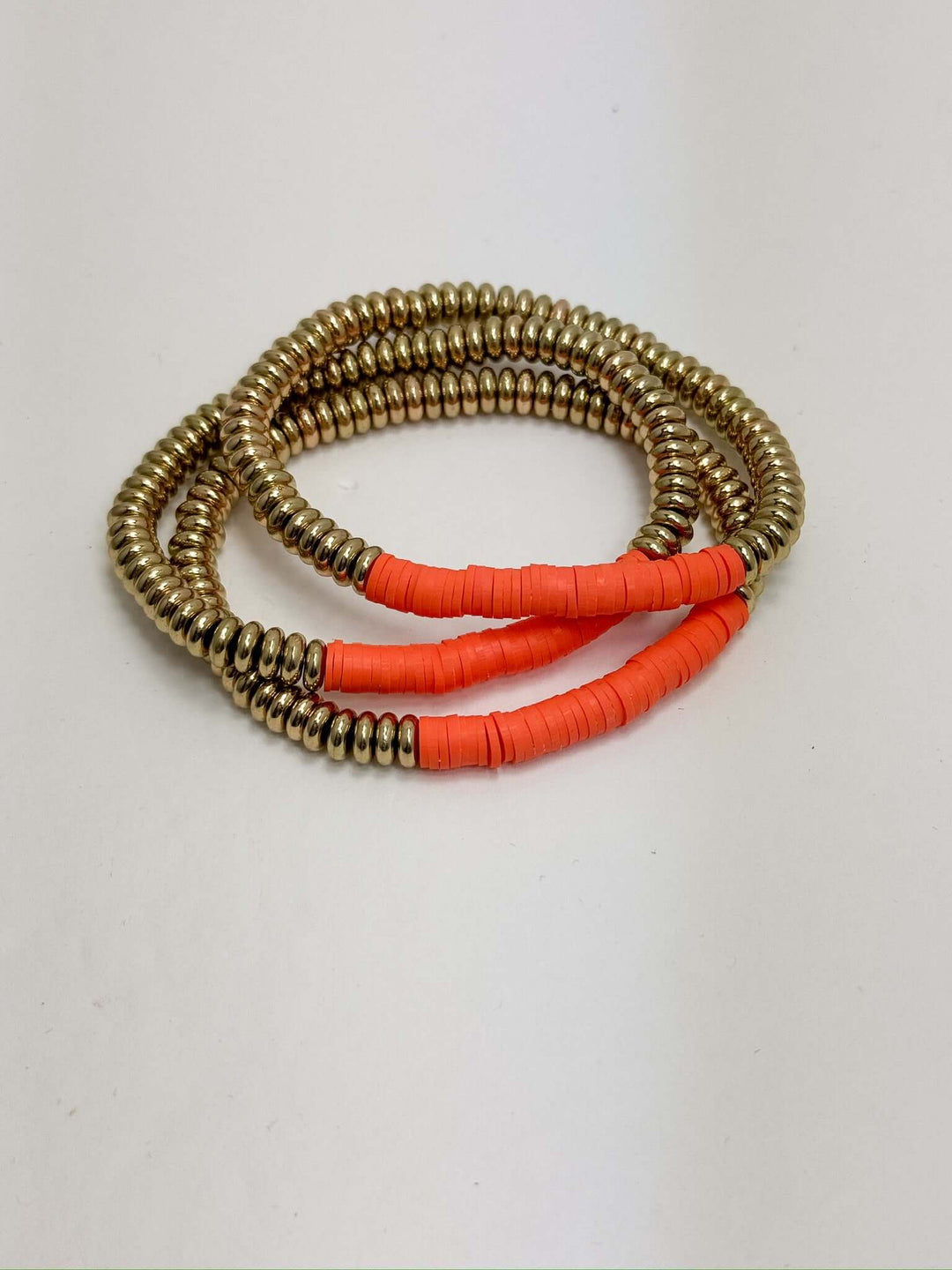A set of three orange and gold bracelets with a tubular bead design, displayed on a white background.