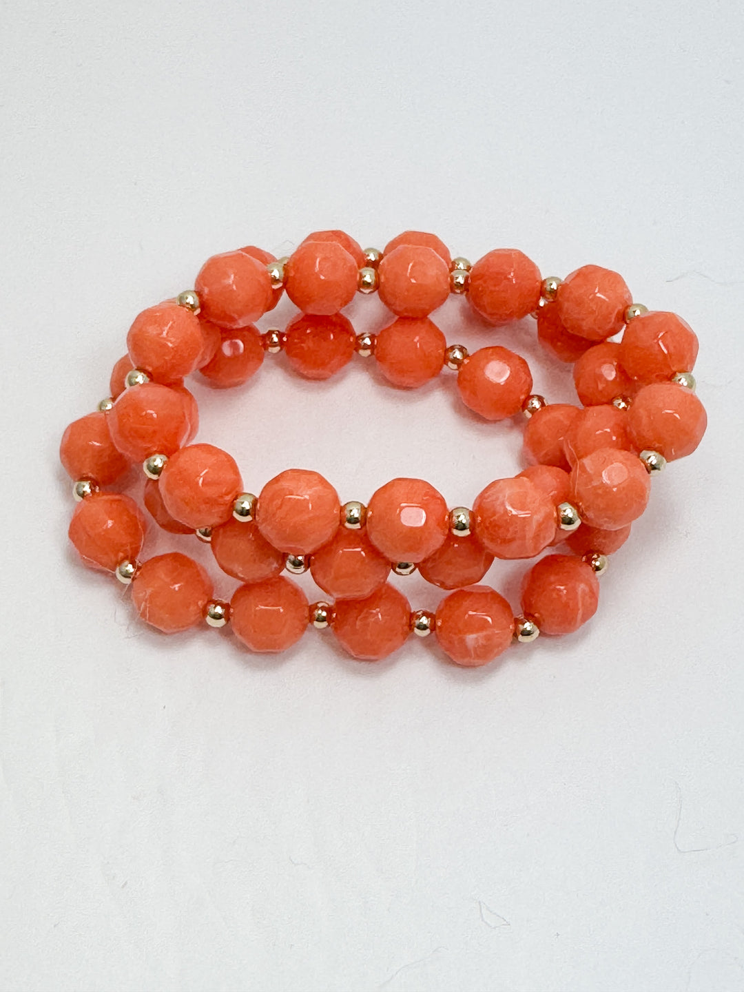 Two coral-colored beaded bracelets on a light gray background