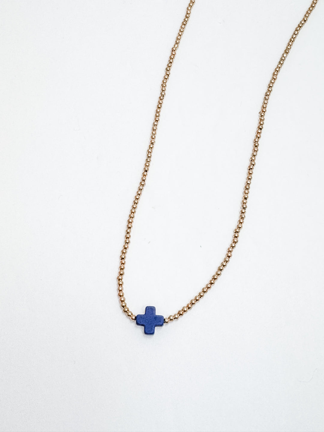 A gold necklace with a navy blue square cross accent, displayed against a white background.
