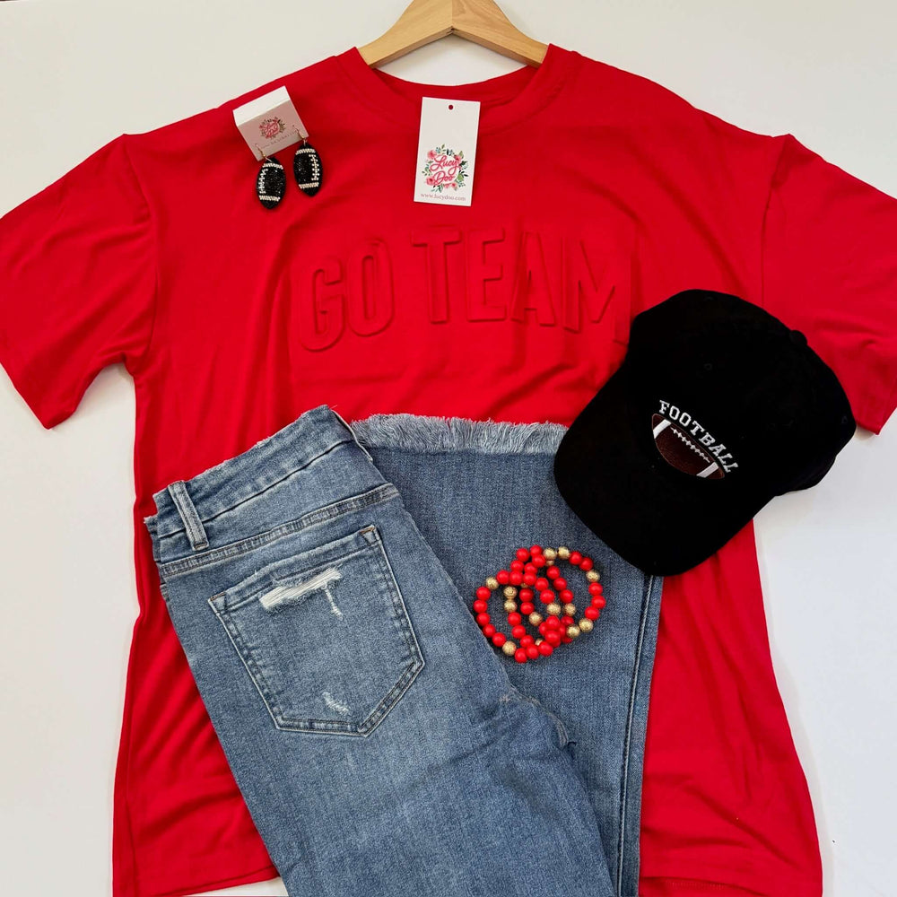 A flatlay photo of a  red 'GO TEAM' t-shirt with embossed text on the front, paired with blue jeans.