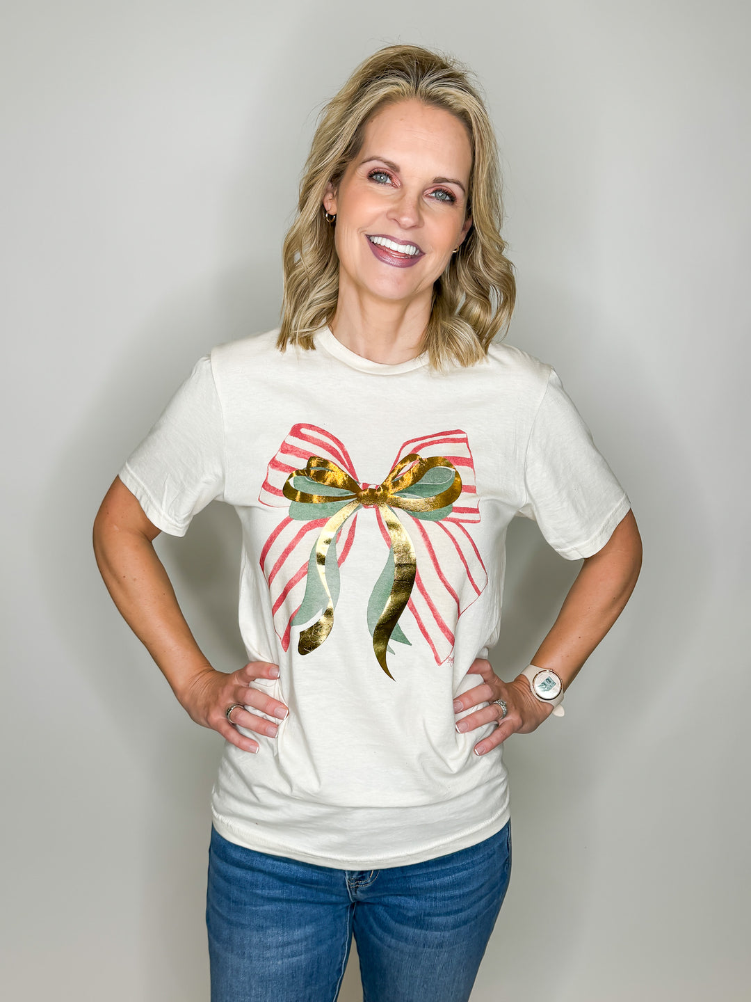 cream tee with red striped green metallic gold bow graphic tee on woman with a white background
