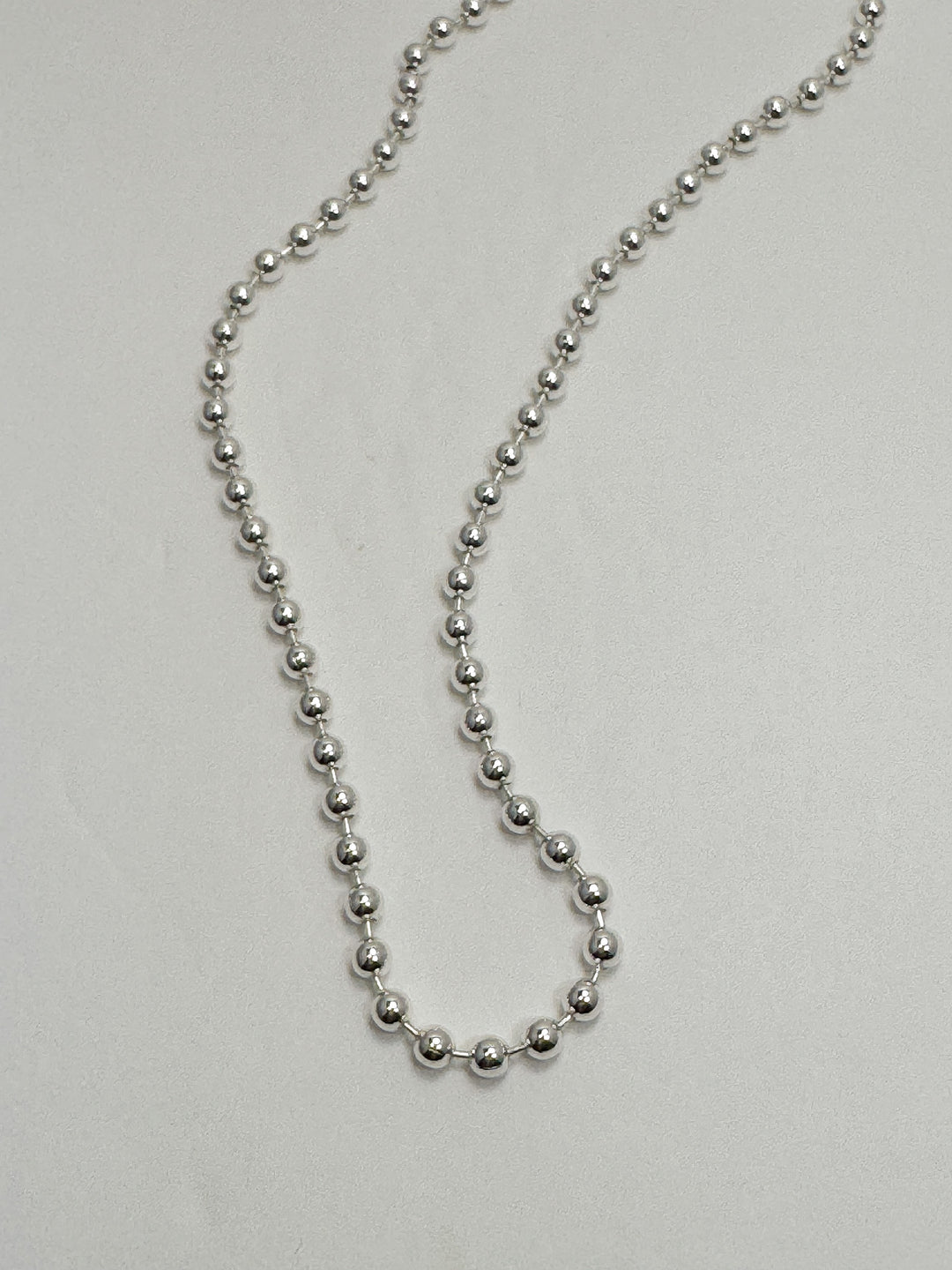 Silver beaded necklace on a light gray background