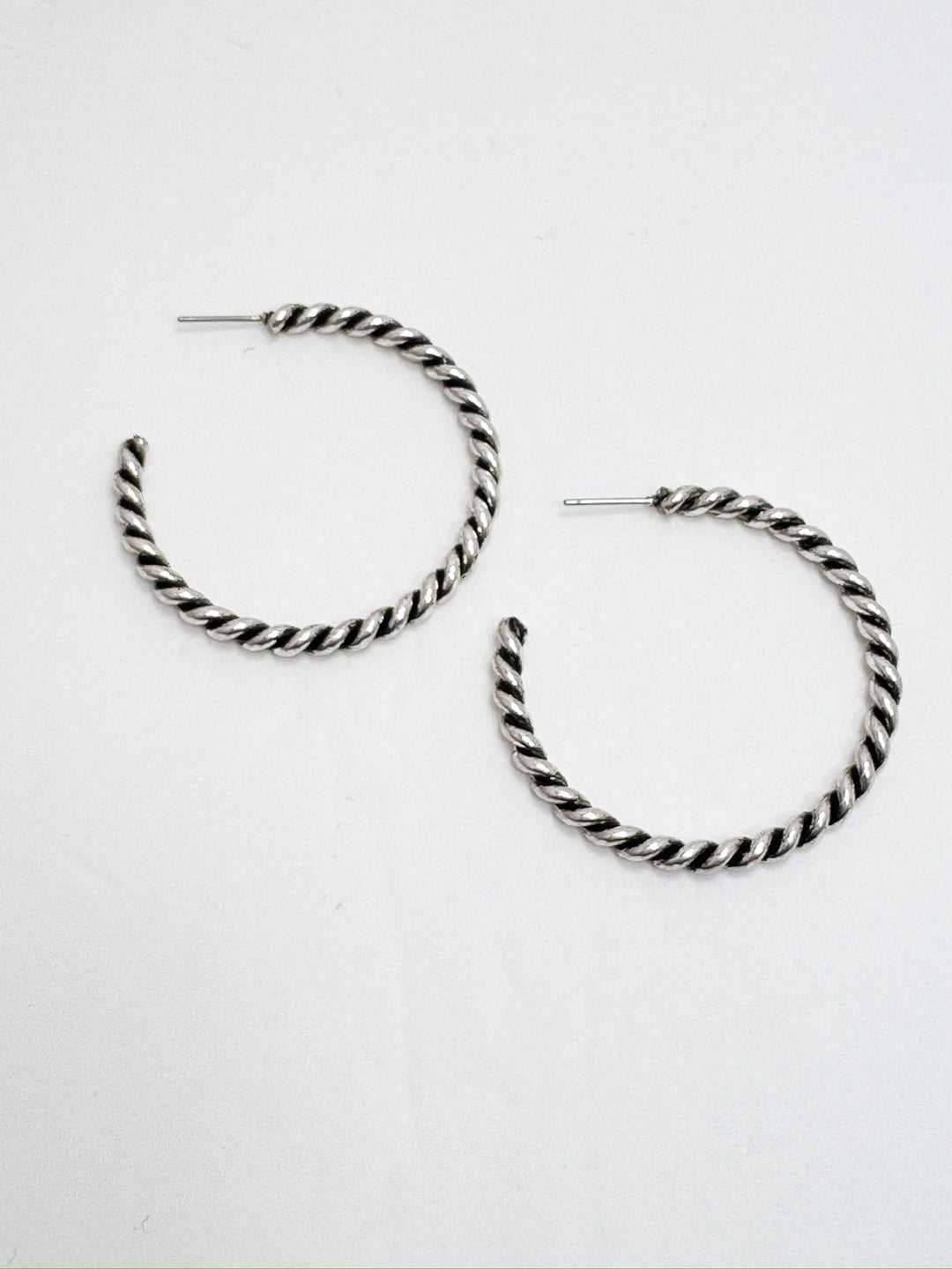 A pair of silver rope hoop earrings on a white background.