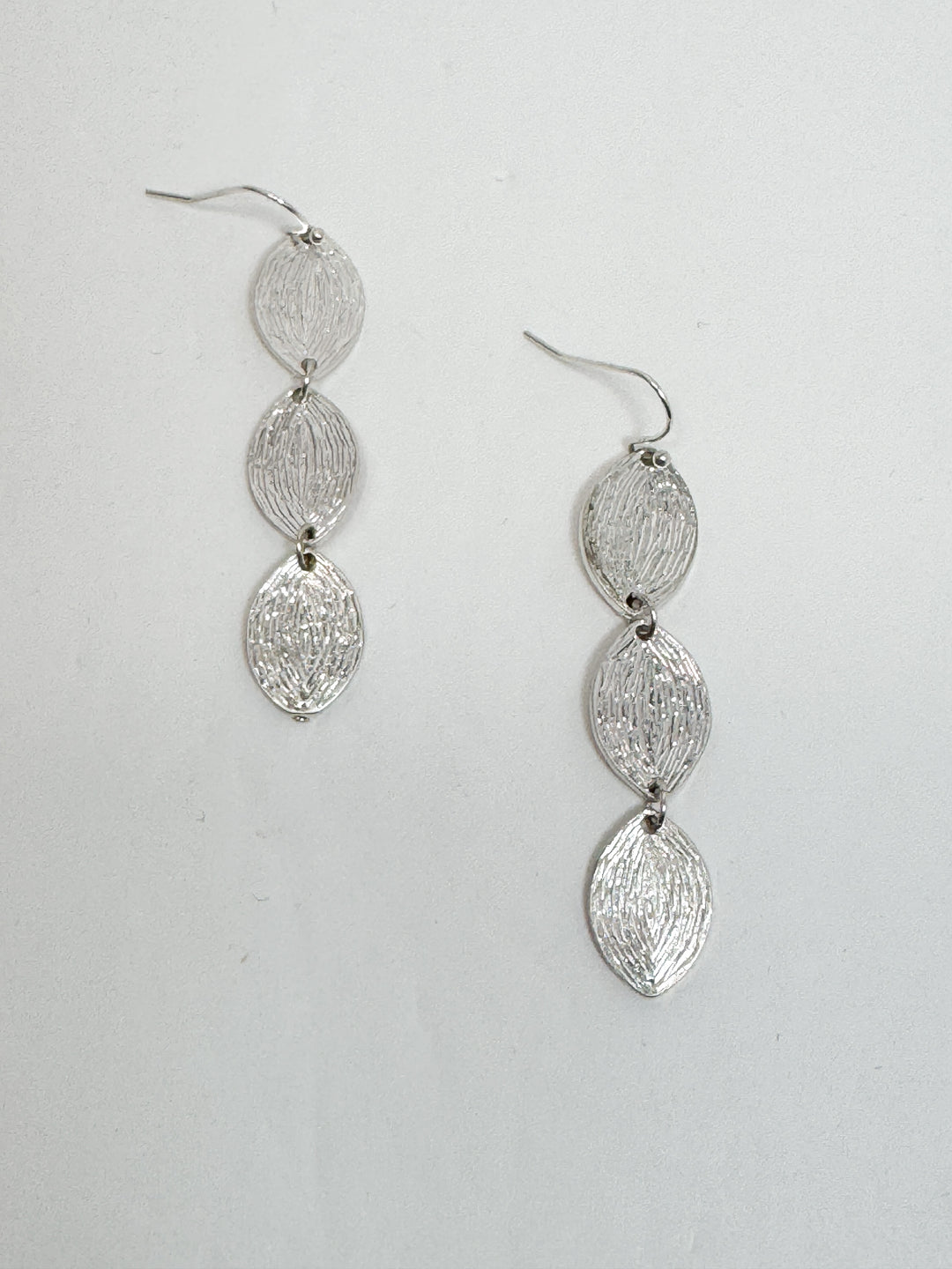Silver earrings with a textured design on a light gray background