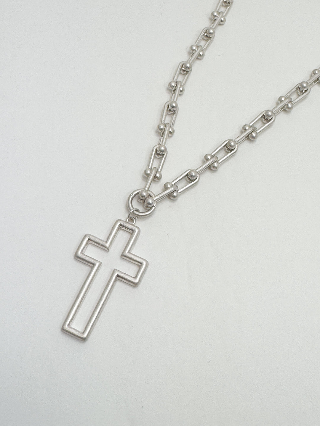 Silver cross pendant on a chain against a white background