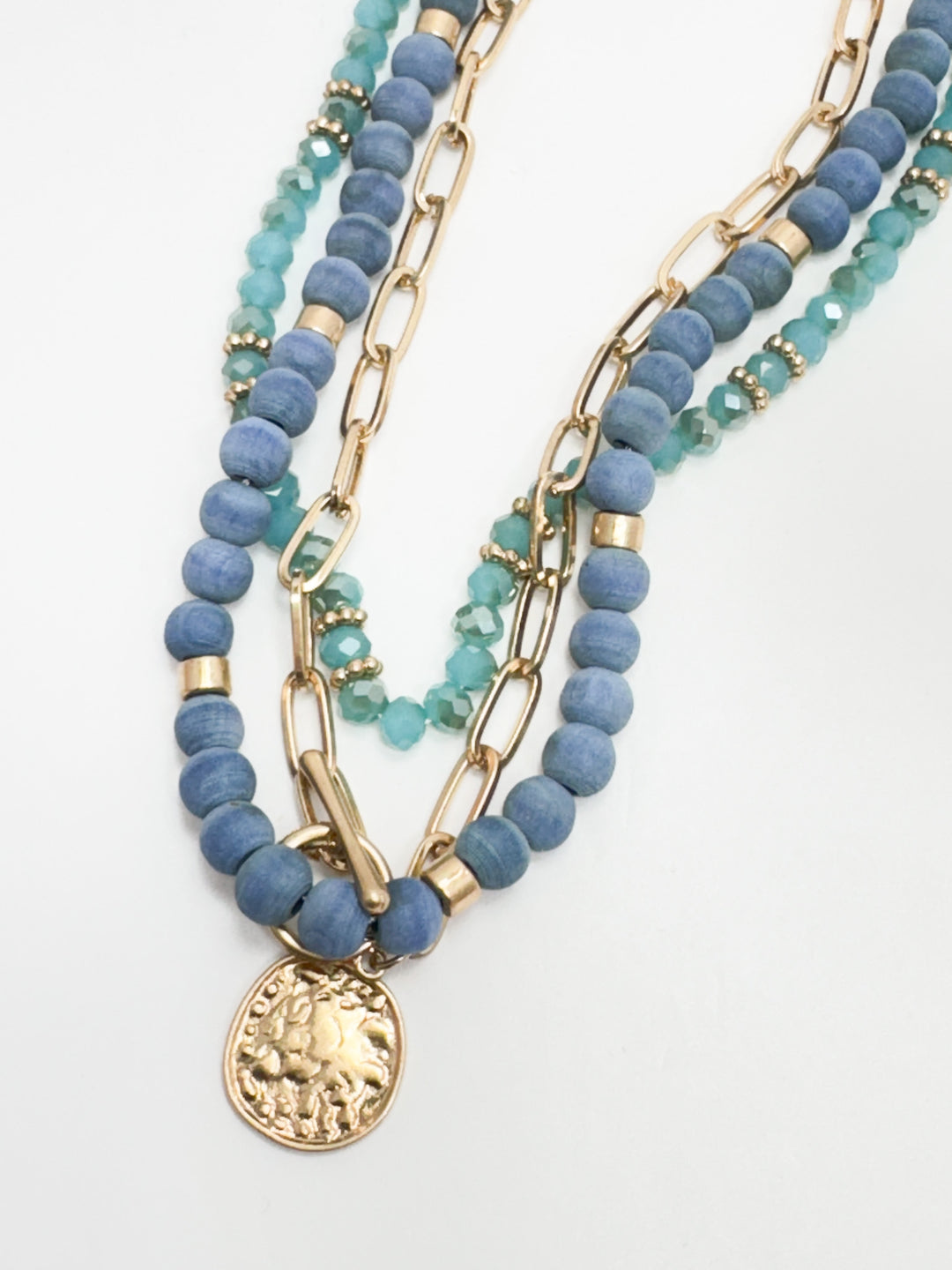 Stack of blue beaded necklaces with gold chain links on a white background