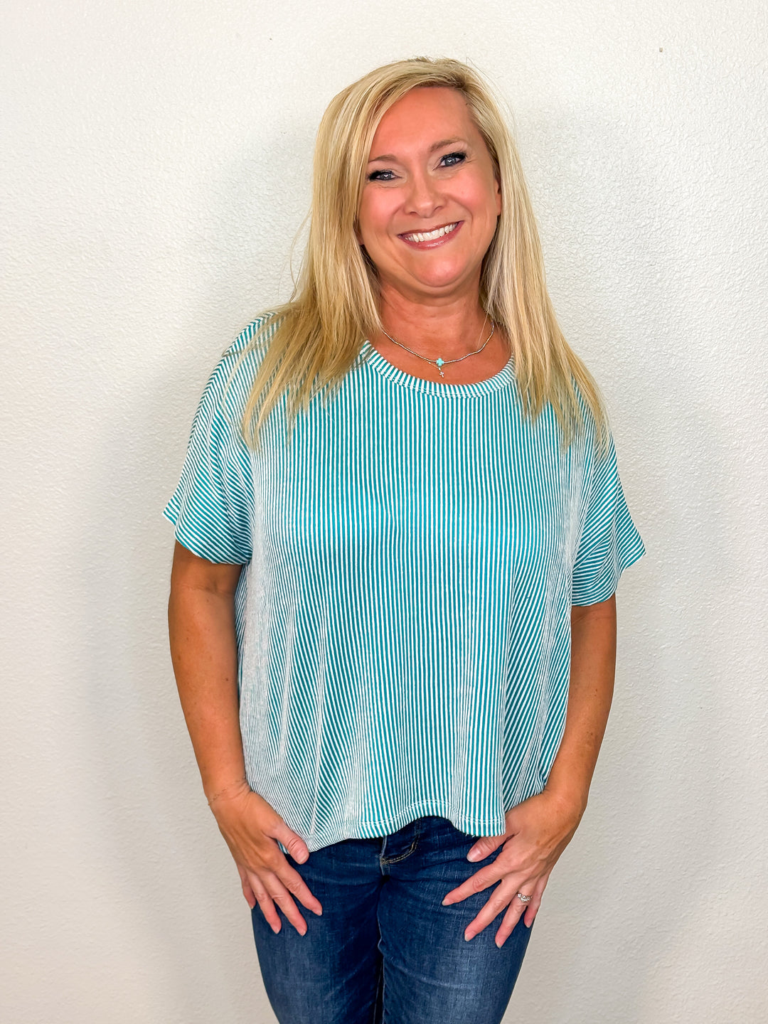 A person wearing a short-sleeved electric teal ribbed top with a round neckline, paired with jeans.