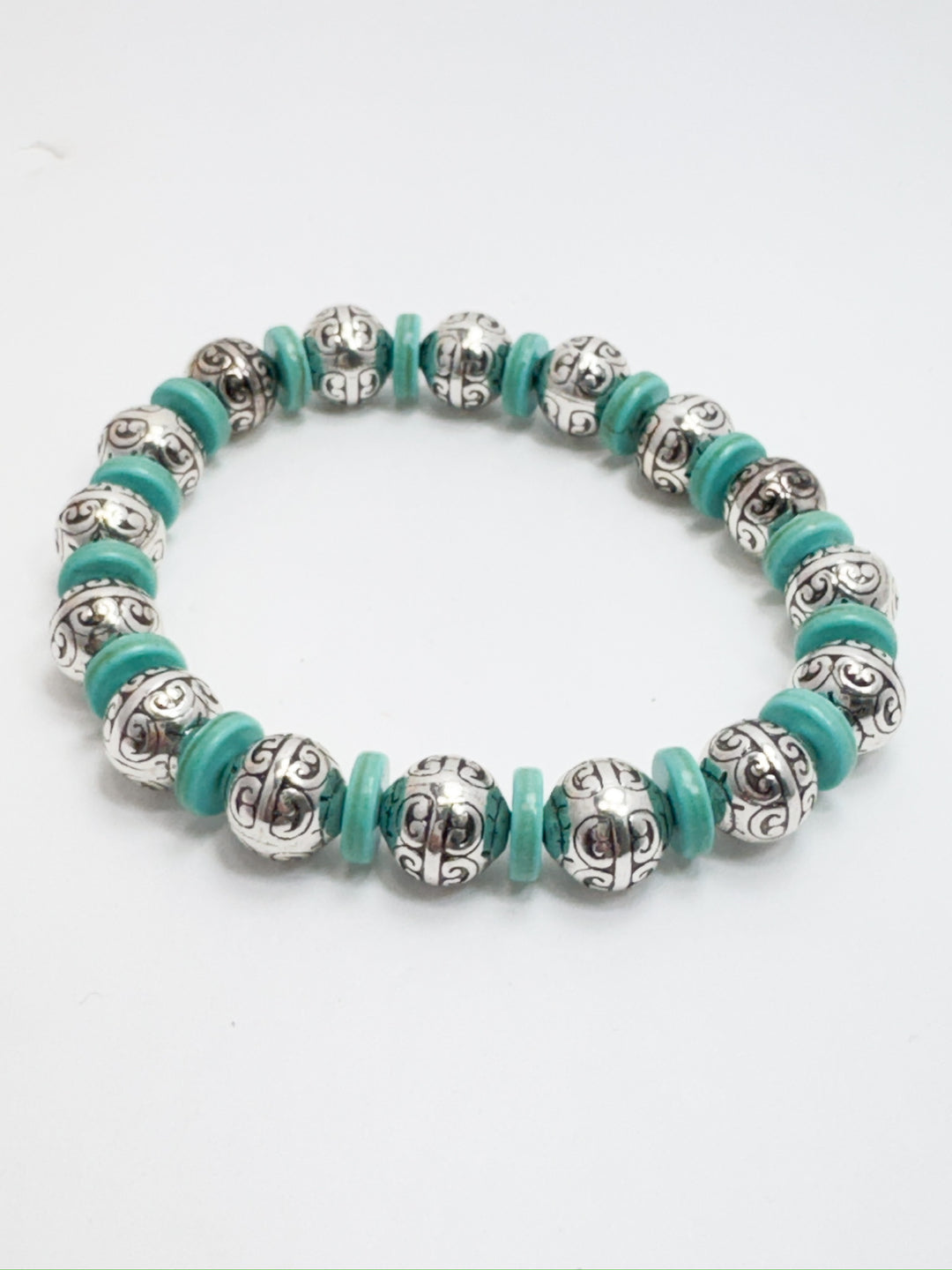 A bracelet with silver filigree and flat turquoise beads, featuring a stretchy design.