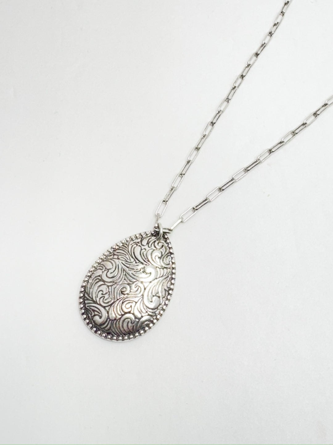 Antique silver tooled pendant on a link silver chain necklace against a white background.