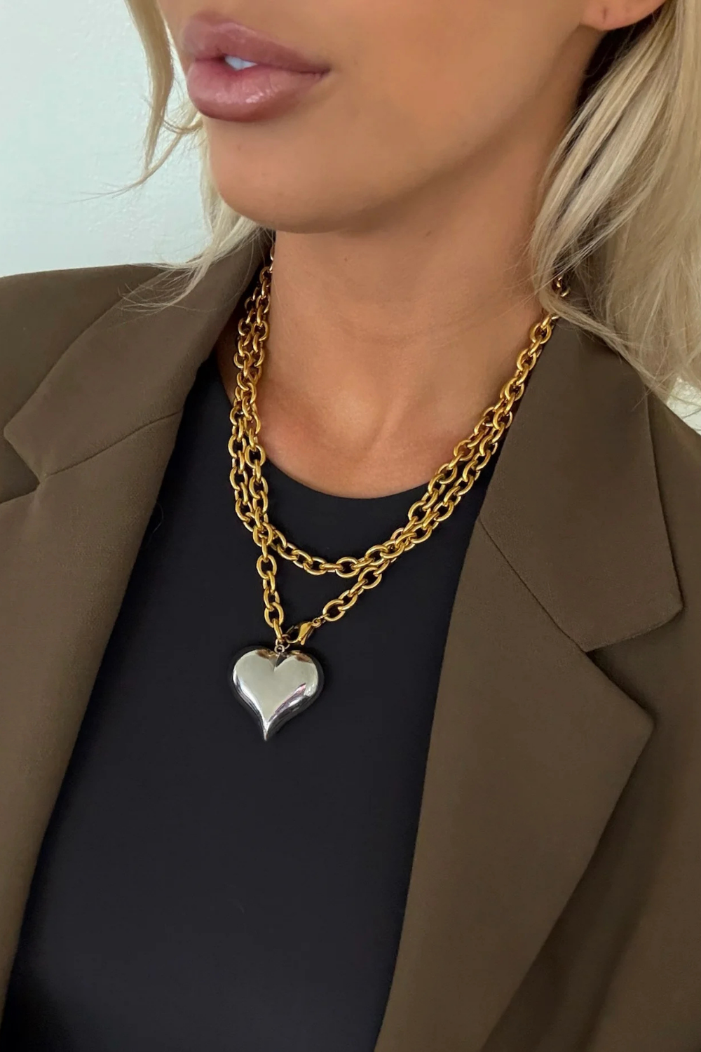 Close-up of a person wearing a gold chain necklace with a heart pendant.