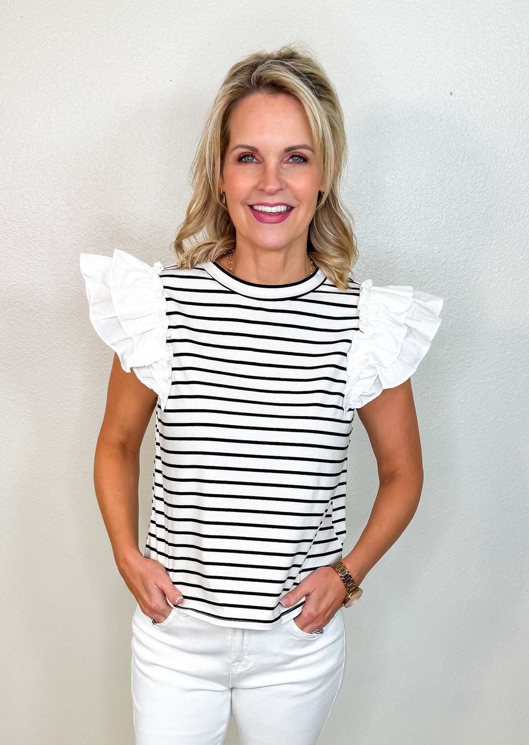 A woman wearing a white and black striped top with double-layered white ruffle flutter sleeves, paired with white pants.