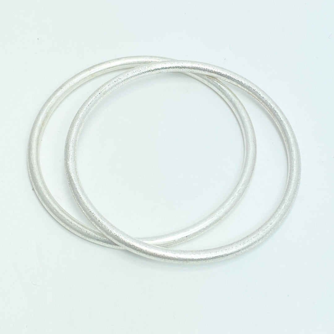 A pair of matte silver bangle bracelets placed together against a white background.