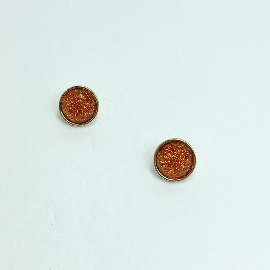 A pair of rust-colored sparkle stud earrings on a white background.