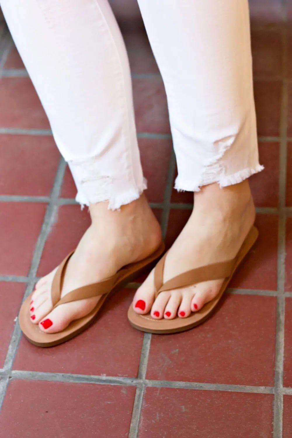 Tan leather flip flops worn on tile floor